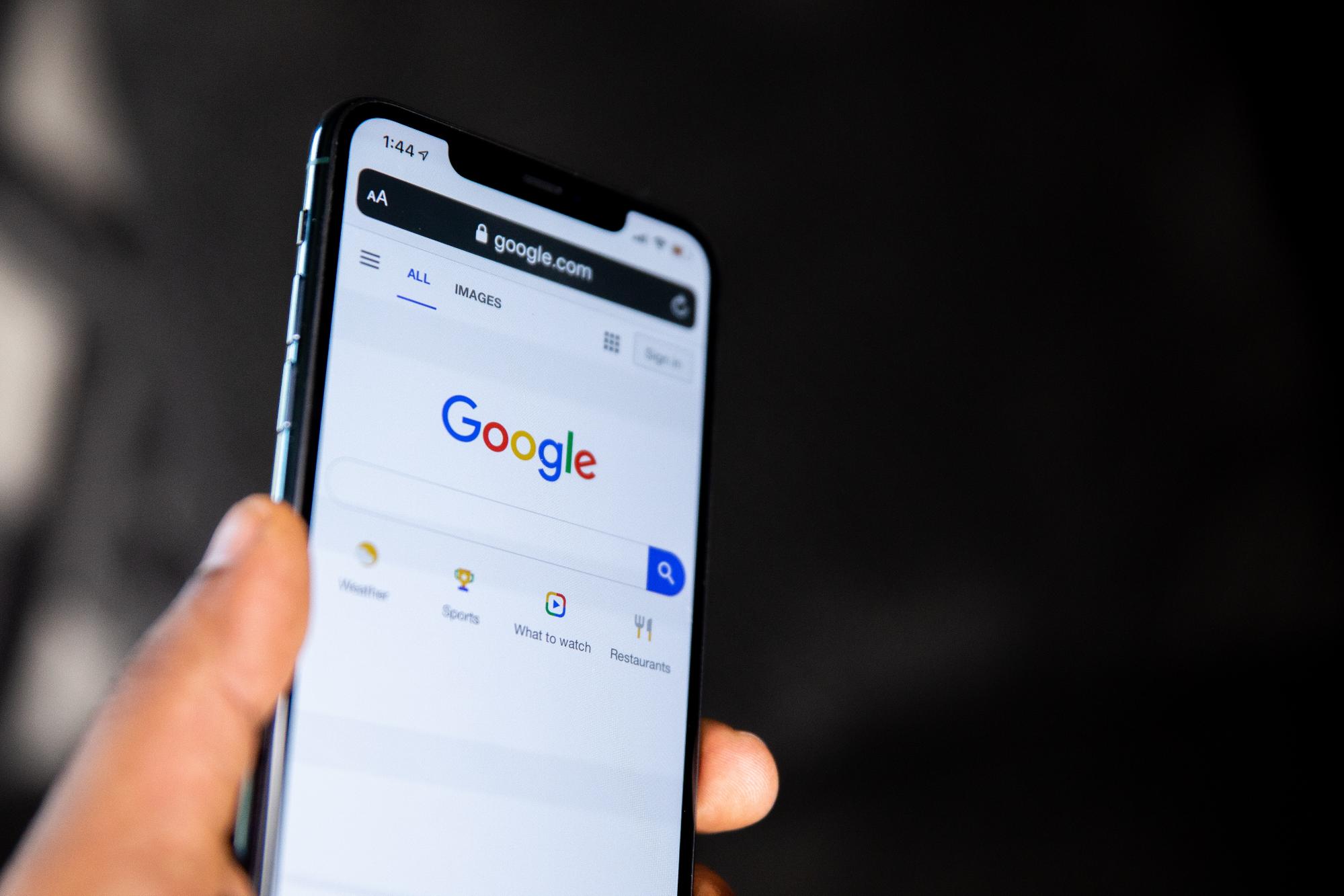 A man's left hand holding a smartphone with Google search pulled up