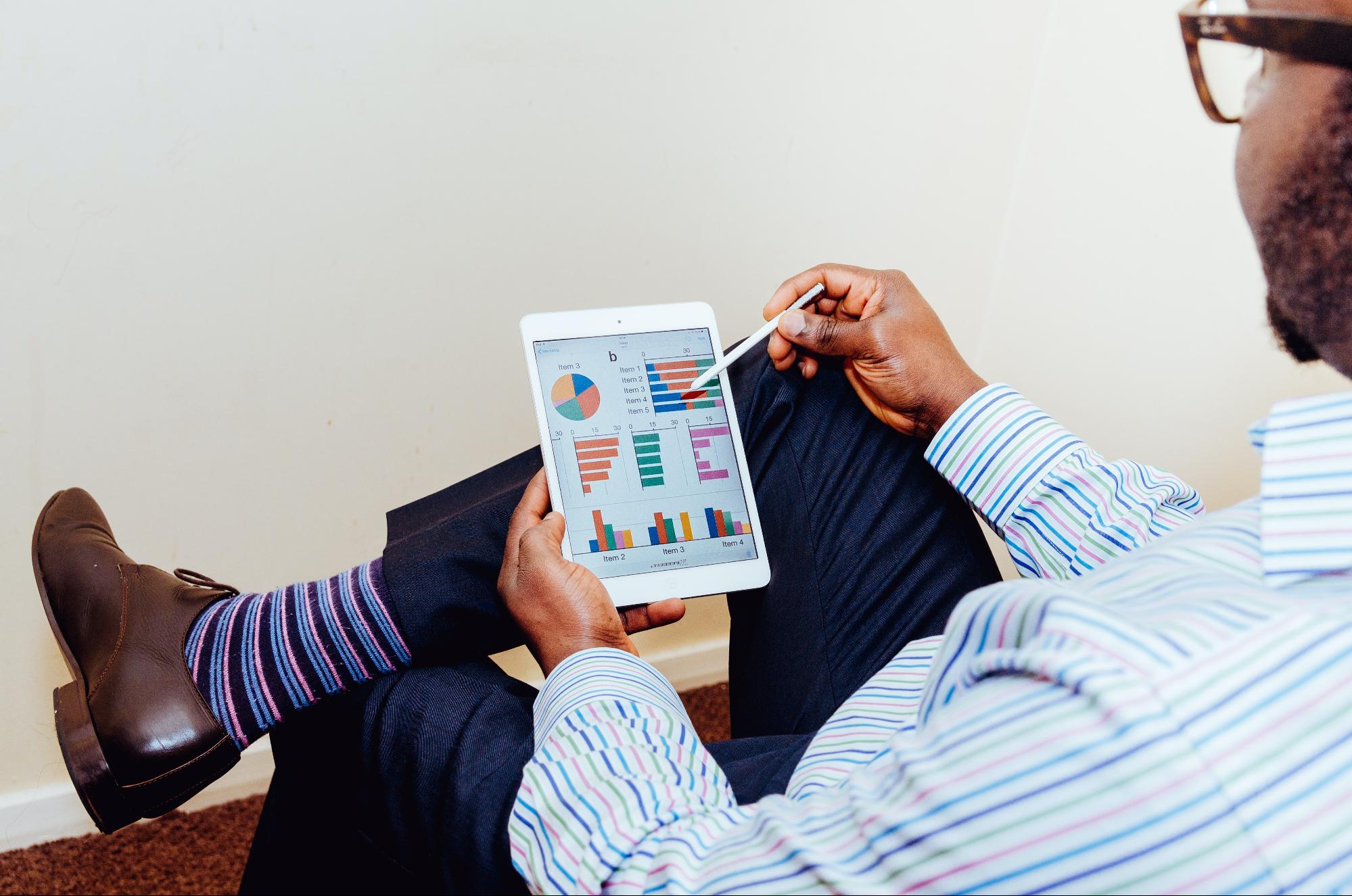 A black man holding a tablet looking over charts and graphs