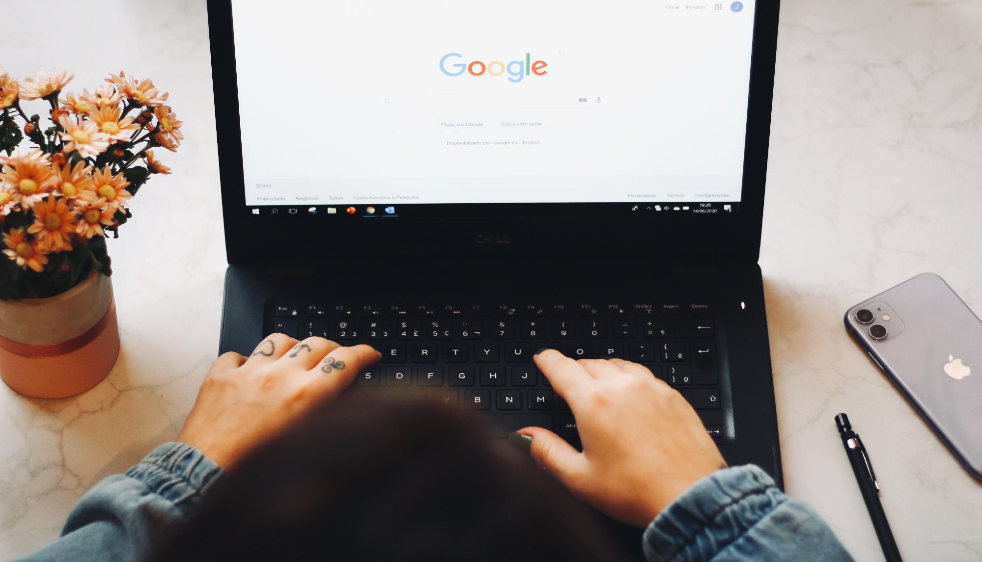 A laptop with hands on the keyboard and Google Search on the screen